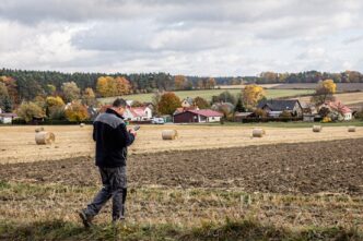 Rolnik na tle jesiennych pól sprawdzający telefon przy gospodarstwie rolnym w Polsce